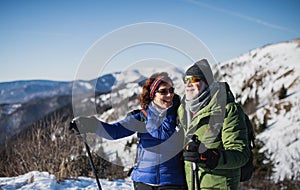 Starší pár turistů s holemi pro nordic walking v zasněžené zimní přírodě.
