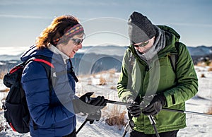 Starší pár turistov s palicami na nordic walking v zasneženej zimnej prírode.