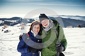 Senior couple hikers with nordic walking poles in snow-covered winter nature.