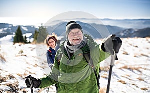 Starší pár turistov s palicami na nordic walking v zasneženej zimnej prírode.