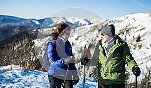 Senior couple hikers with nordic walking poles in snow-covered winter nature.