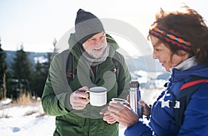 Senior couple hikers in snow-covered winter nature, drinking hot tea.