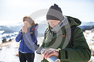 Senior couple hikers in snow-covered winter nature, drinking hot tea.