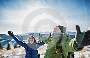 Starší pár turistů v zasněžené zimní přírodě, natahování rukou.