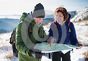 Senior couple hikers using map in snow-covered winter nature.