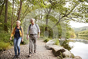 Senior Couple Hiking Along Path By River In UK Lake District