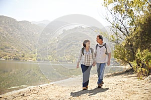 Senior couple hold hands hiking by a mountain lake