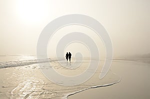 Senior couple holding hands walking on beach enjoying sunrise.