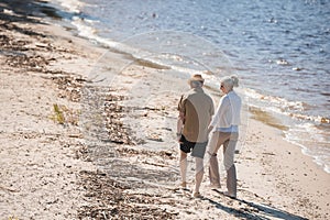 Senior couple holding hands and walking on sand at riverside