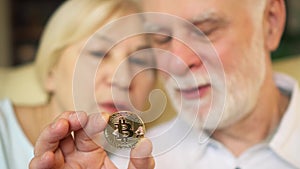 Senior couple holding and looking at cryptocurrency bitcoin. Shiny virtual money of online trade