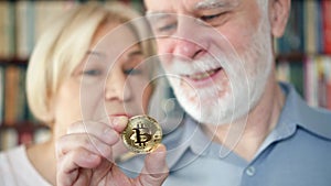 Senior couple holding and looking at cryptocurrency bitcoin. Shiny virtual money of online trade