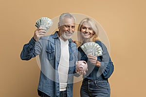 Senior couple holding money and piggy bank, isolated on beige