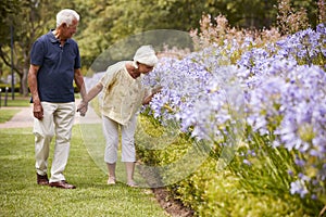 Senior Couple Holding Smelling Flowers On Walk In Park Together