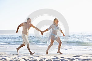 Senior Couple On Holiday Running Along Sandy Beach Looking Out To Sea