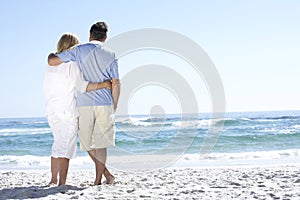 Senior Couple On Holiday Walking Along Sandy Beach Looking Out To Sea