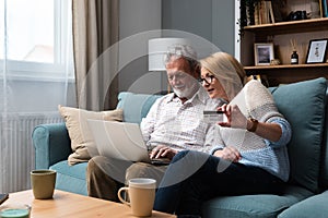 Senior couple at home. Handsome older man and attractive older woman are spending time together. Sitting on a sofa with laptop