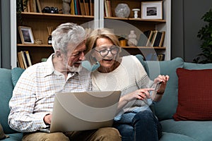 Senior couple at home. Handsome older man and attractive older woman are spending time together. Sitting on a sofa with laptop