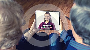 Senior couple at home holding digital tablet during video call with family doctor in telehealth