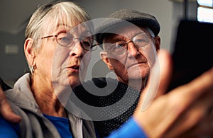 Senior Couple At Home Making Video Call To Family On Mobile Phone
