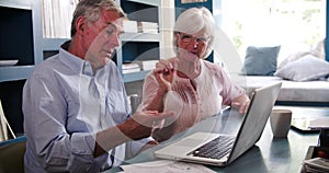 Senior Couple In Home Office Looking At Laptop And Arguing