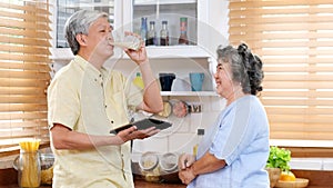 Senior couple at home, Old asian man drinking milk at kitchen standing with old woman, Elderly asia male holding glass of milk for