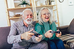 Senior couple at home playing video game holding joysticks in hands