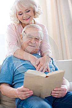 Senior couple hugging and relaxing, man reading book