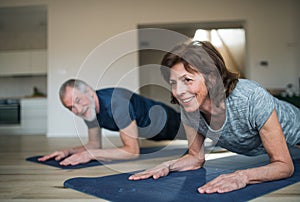 A senior couple indoors at home, doing exercise on the floor.