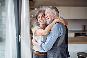 A senior couple indoors at home, looking out of window.