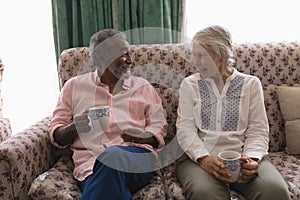 Senior couple interacting with each other while having coffee in living room