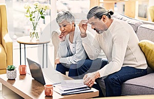 Senior couple, laptop and financial crisis on sofa with documents in budget struggle or debt at home. Frustrated elderly