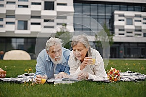 Senior couple laying on a blanket on a picnic in summer and reading a book