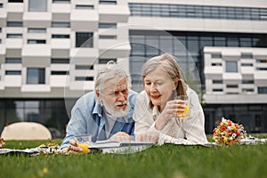 Senior couple laying on a blanket on a picnic in summer and reading a book