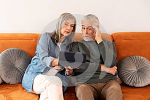 Senior Couple Learning On Digital Tablet While Sitting On Sofa