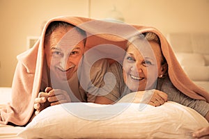 Senior couple lie together under the covers.