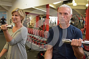 Senior couple lifting dumbbells while sitting at gym