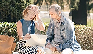 Senior couple looking sad and disappointed while using a laptop in a sunny park