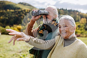 Senior couple looking at view trough binoculars on autumn walk.