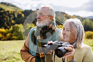 Senior couple looking at view trough binoculars on autumn walk.