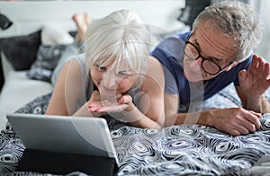 Senior couple lying on bed having video conversation