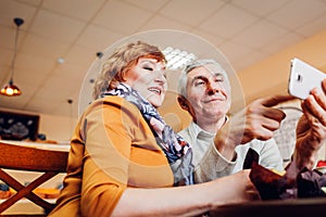 Senior couple makes a selfie using a smartphone in cafe. Celebrating anniversary. Retired people having fun