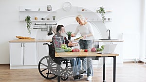 Senior couple, man in wheelchair and elderly woman, making healthy salad.