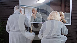 Senior couple man and woman brushing teeth and looking into a mirror at luxury bathroom at home