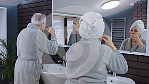 Senior couple man and woman brushing teeth and looking into a mirror at luxury bathroom at home