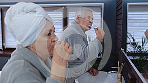 Senior couple man and woman brushing teeth and looking into a mirror at luxury bathroom at home