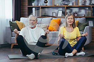 Senior couple man and woman together at home practicing yoga meditating sitting on the floor in lotus position