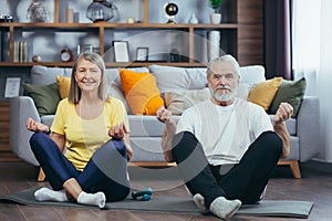 Senior couple man and woman together at home practicing yoga meditating sitting on the floor in lotus position
