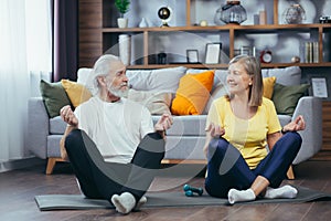 Senior couple man and woman together at home practicing yoga meditating sitting on the floor in lotus position