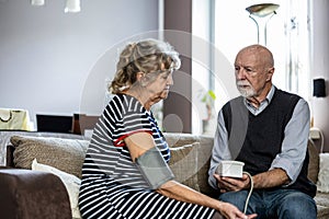 Senior couple measuring blood pressure while sitting on sofa