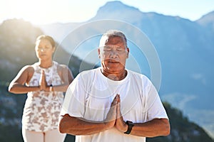 Senior couple meditating with joined hands and closed eyes breathing deeply. Mature couple doing yoga in nature living a